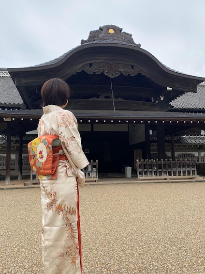 A person in traditional attire standing in front of a temple with a distinctive roof and a clock. 4