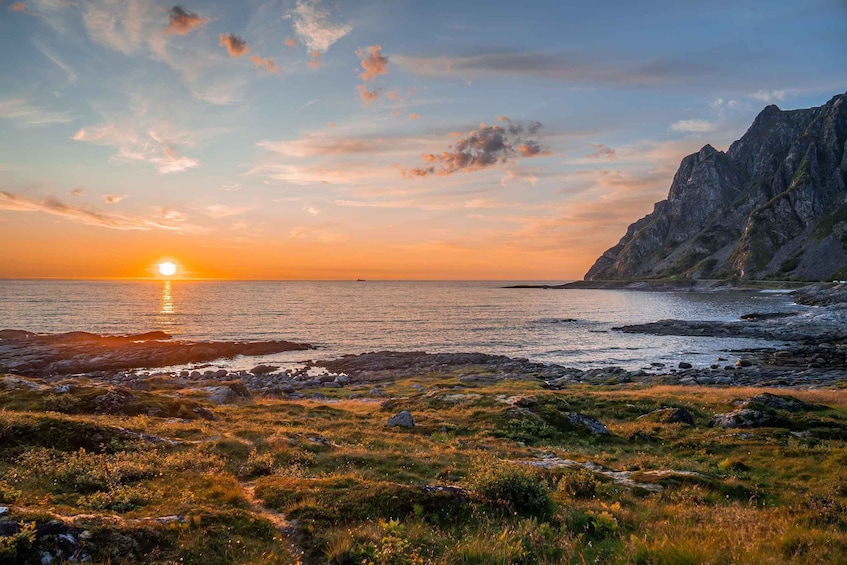 A sunset over a rocky coastline with a mountain in the background. 1
