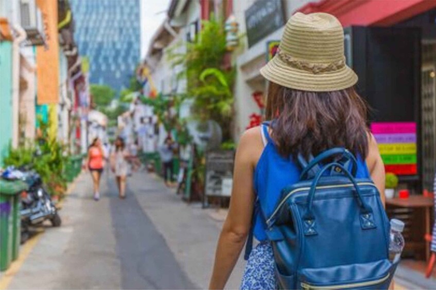 A person walking down a street with buildings on either side, a blue backpack, and a straw hat. 3