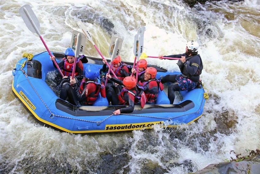 A group of people in a blue inflatable raft navigating a river with rapids. 1