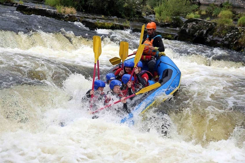 A group of people in a blue raft navigating through a river with rapids. 2