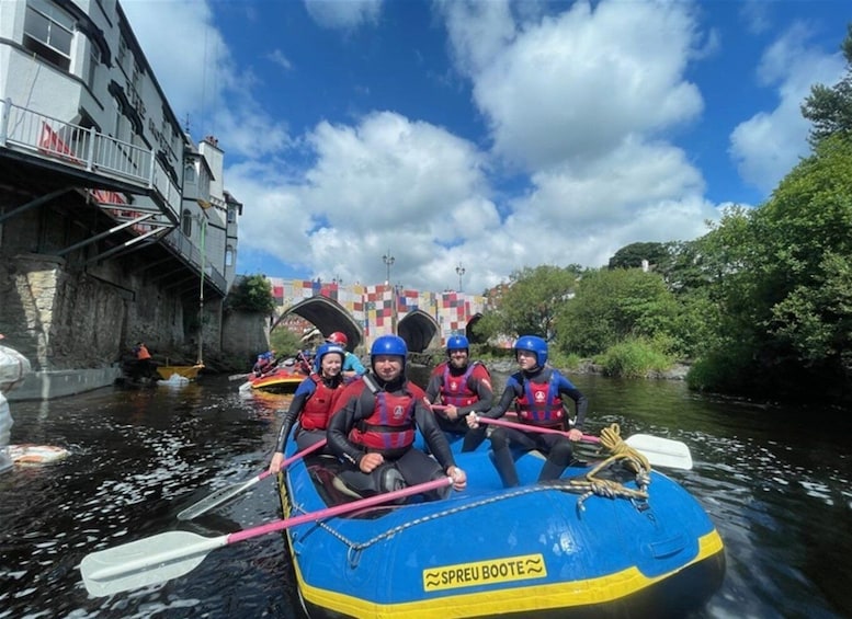A group of people in a blue raft with paddles, navigating a narrow waterway. 3
