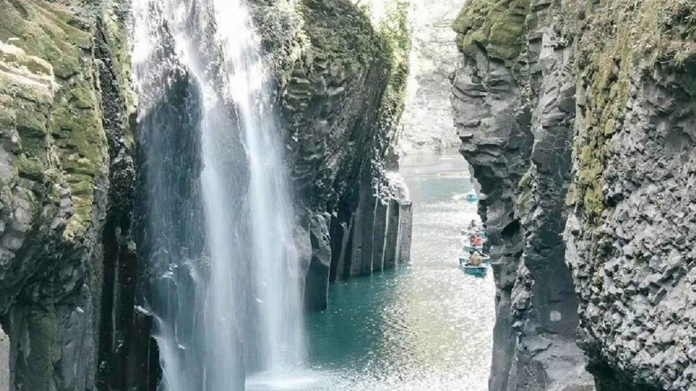 A waterfall cascading down a rocky gorge with a boat visible in the water below. 2