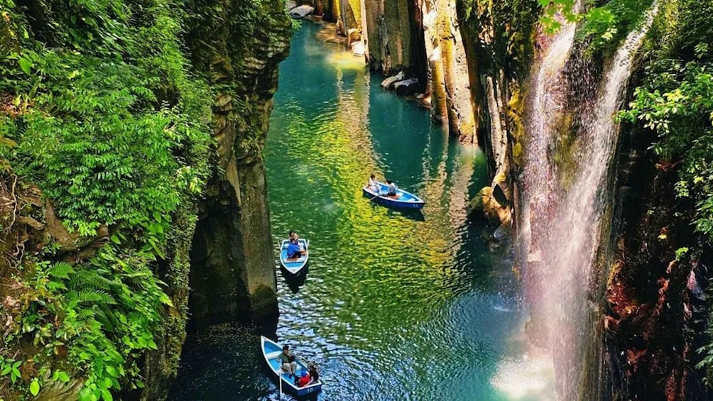A narrow waterway flanked by tall cliffs, with two boats and a waterfall. 3