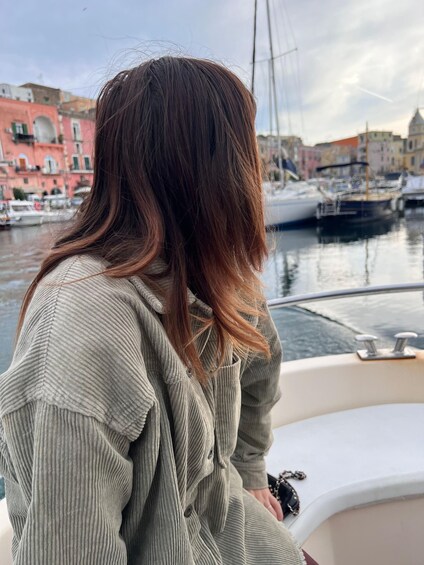 A person with long hair sitting on a boat, looking at a marina with buildings in the background. 2