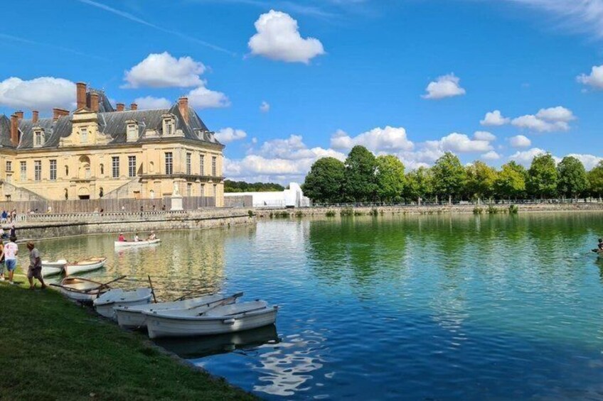 A calm river with boats docked, a historic building, and a clear sky. 3