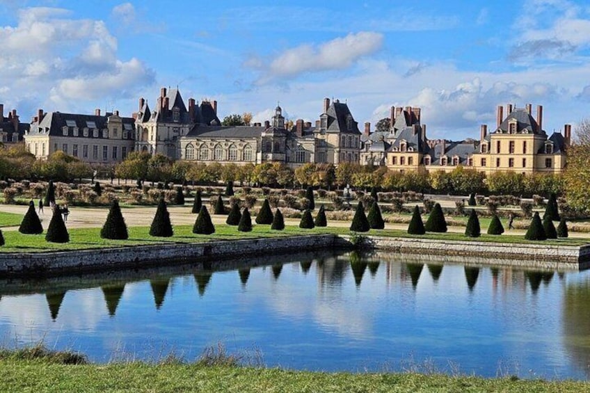 A historic building complex with a reflective water body and neatly trimmed topiary. 4