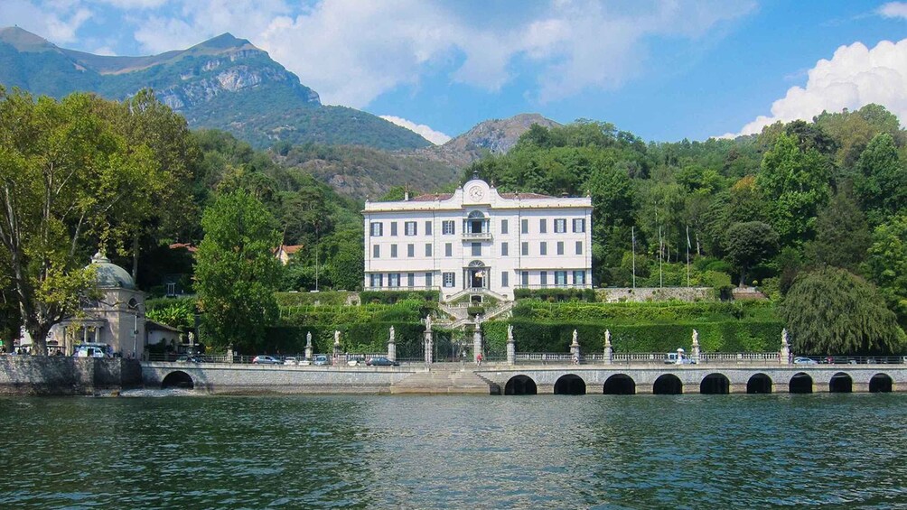 A large white building with a clock tower, surrounded by lush greenery and mountains in the background. 2