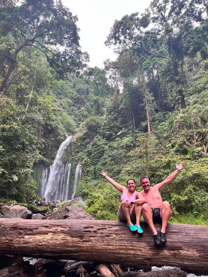A couple sitting on a log by a waterfall in a forest. 3