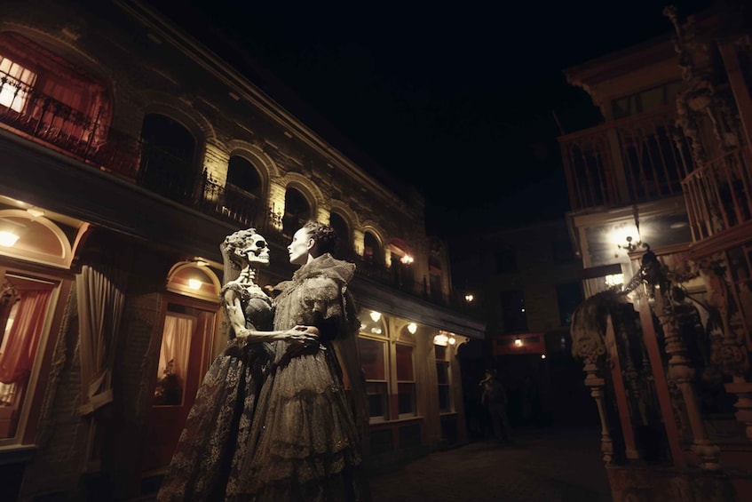 A nighttime scene with a statue of a woman holding a skull, set against a backdrop of a historic building with arched windows and ornate details. 1
