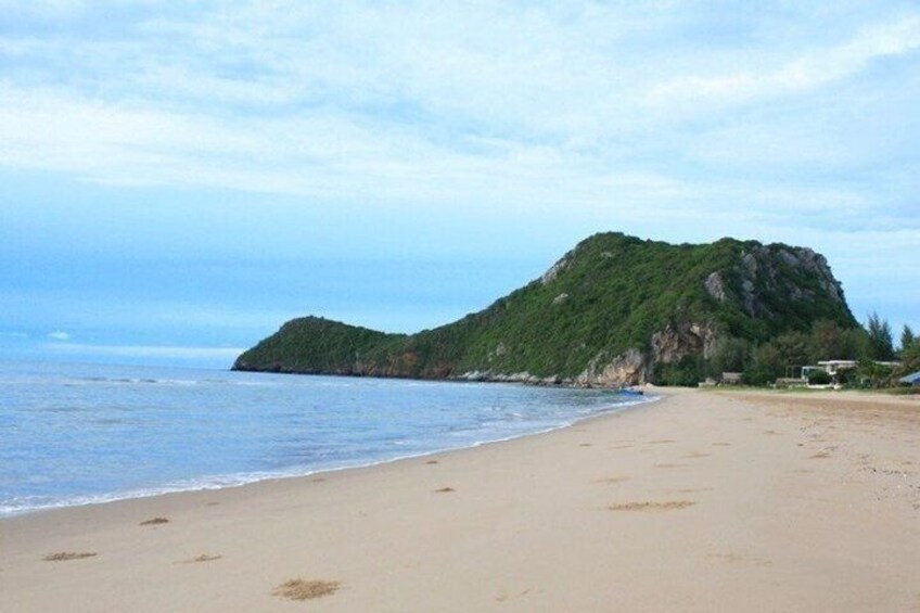 A beach with a sandy shore, a large green hill, and a clear sky. 2