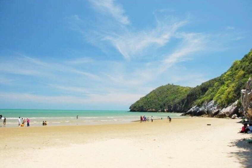 A beach with people, a clear sky, and a green hill in the background. 3