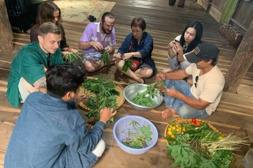 A group of people sitting on the floor, engaged in a communal activity with various plants and vegetables. 1