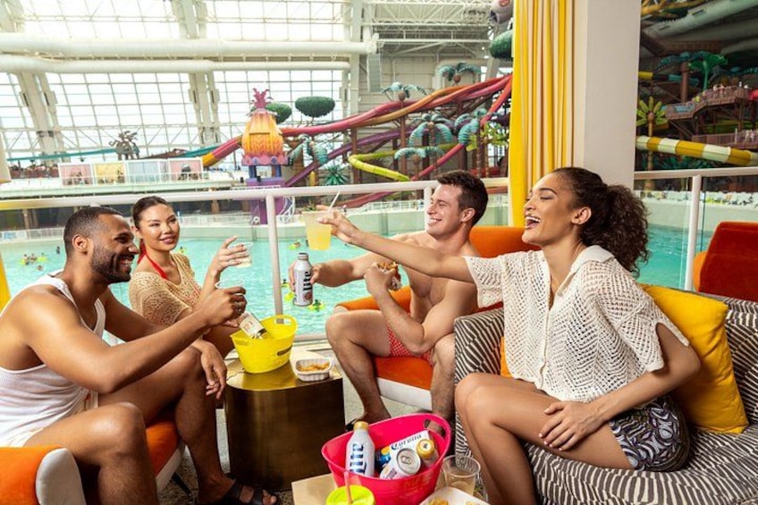 A group of people sitting by a poolside, with water slides and a large indoor water park in the background. 2