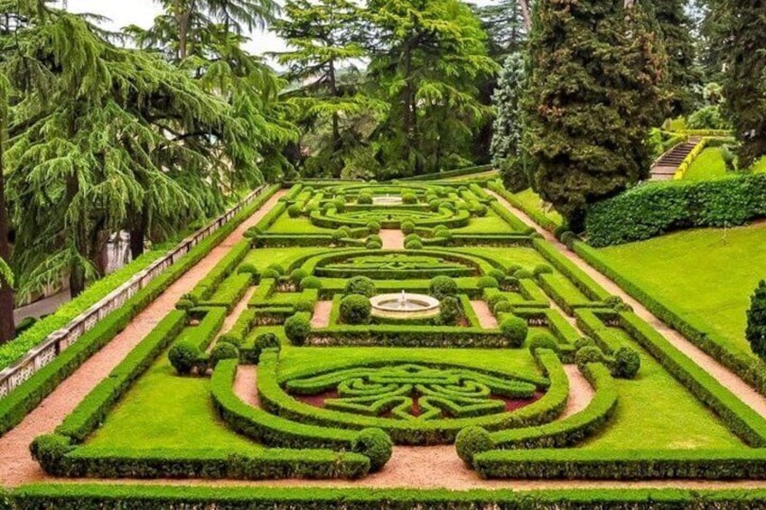 A formal garden with geometric hedges, a central circular feature, and a variety of trees. 2