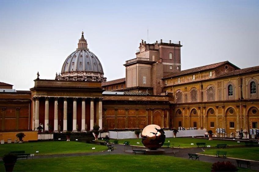 A large building with a dome, columns, and a spherical sculpture in the foreground. 1