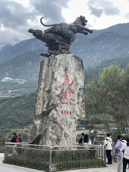 A rock with a tiger statue and text, surrounded by a metal fence, with mountains in the background. 4
