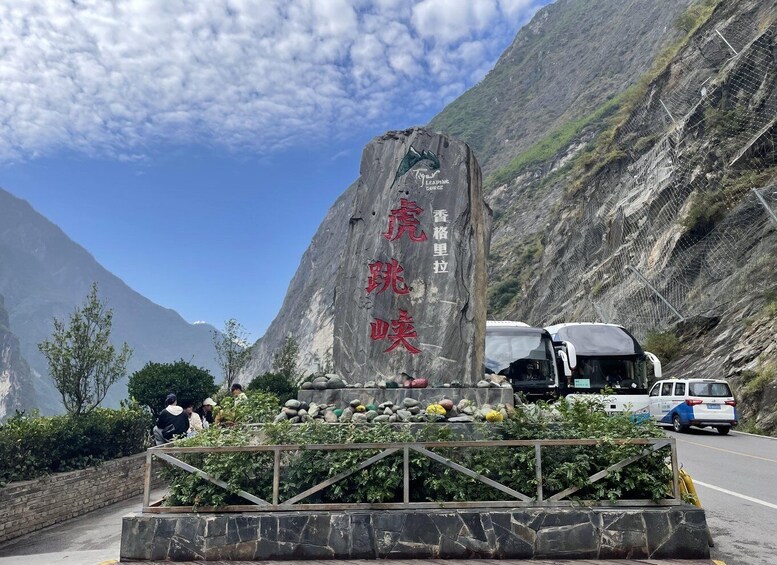 A large rock monument with inscriptions, surrounded by greenery and a mountainous backdrop. 5