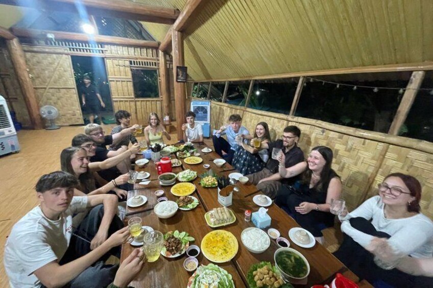 A group of people sitting around a wooden table with various dishes and drinks. 2