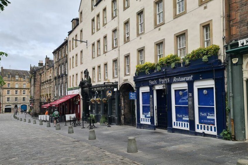 A cobblestone street with a blue building labeled 'Petit Paris Restaurant' and a statue in the foreground. 2