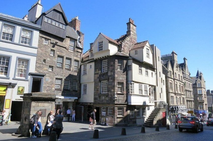A cobblestone street with historic buildings, a pedestrian area, and a car parked on the side. 3
