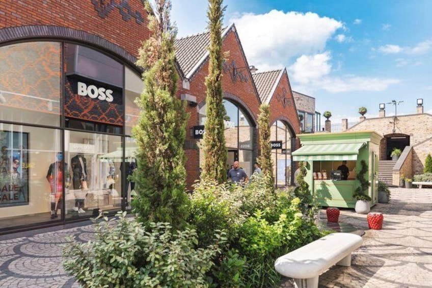 A commercial area with a Boss store, a green kiosk, and a brick building. 1