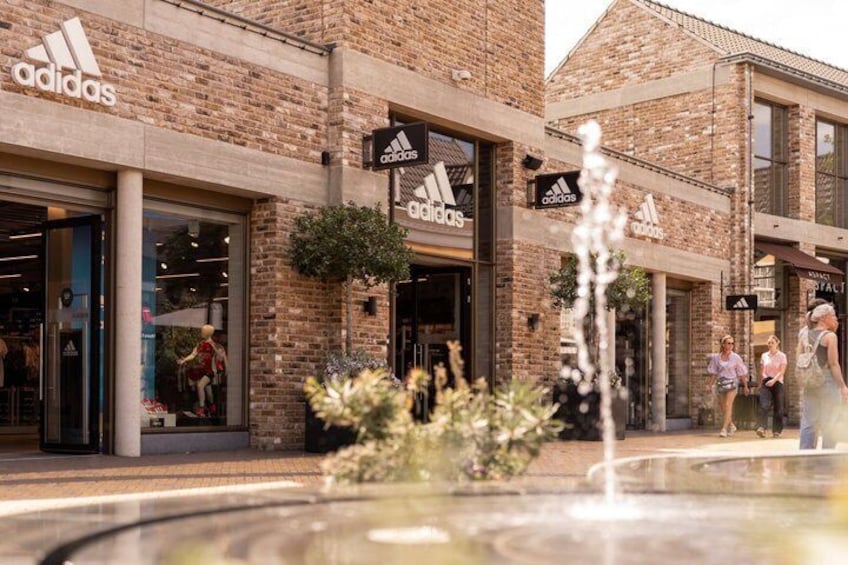 An Adidas store with a brick facade, a fountain in the foreground, and pedestrians in the background. 4