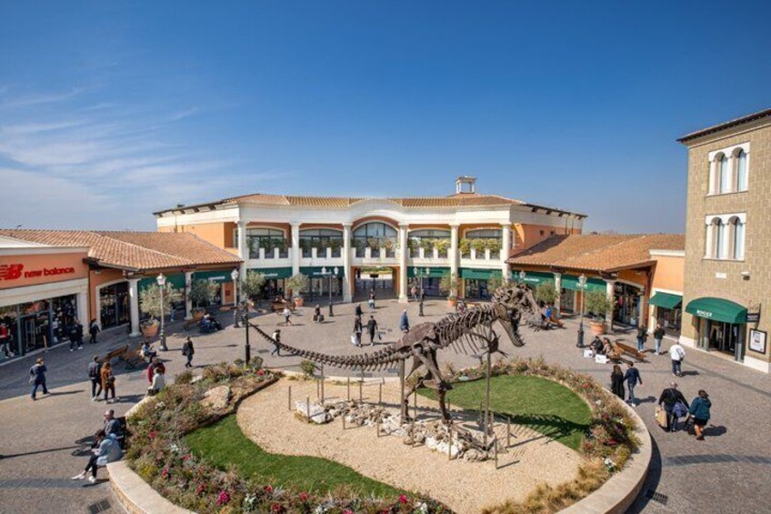 A dinosaur skeleton in a plaza with shops and a building in the background. 3