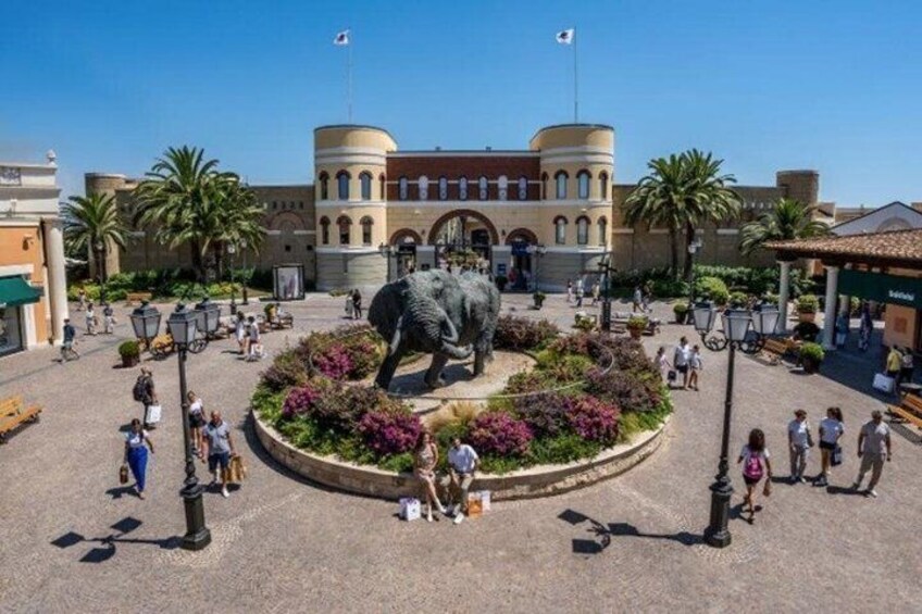 A plaza with a large elephant statue, palm trees, and a building with arched windows. 5