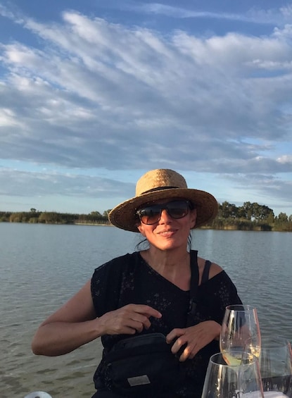 A person wearing a straw hat and sunglasses, sitting by a lake with a clear sky. 2
