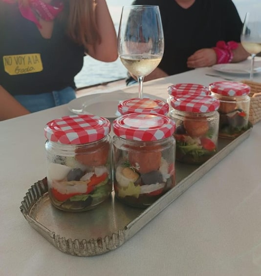 A tray with six glass jars containing layered food, a wine glass, and people in the background. 5