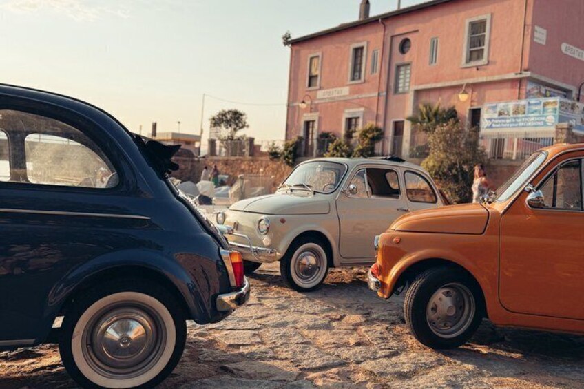 Three vintage cars parked on a cobblestone street with a red building in the background. 3