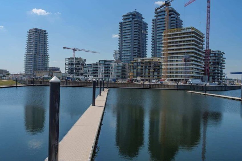 A waterfront with a dock extending into calm water, surrounded by high-rise buildings under construction with cranes. 2