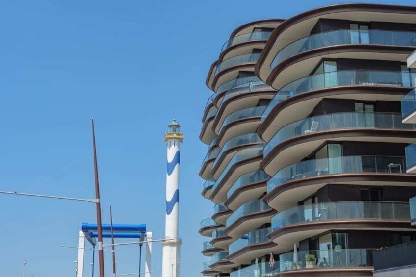 A modern building with curved balconies and a lighthouse in the background. 3