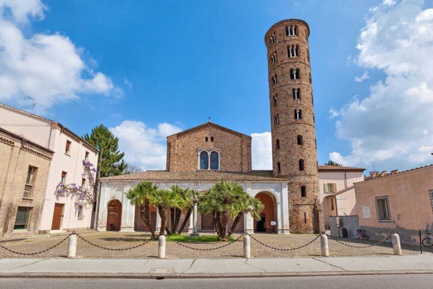 A historic building with a tall tower, arched windows, and a paved courtyard with palm trees. 4
