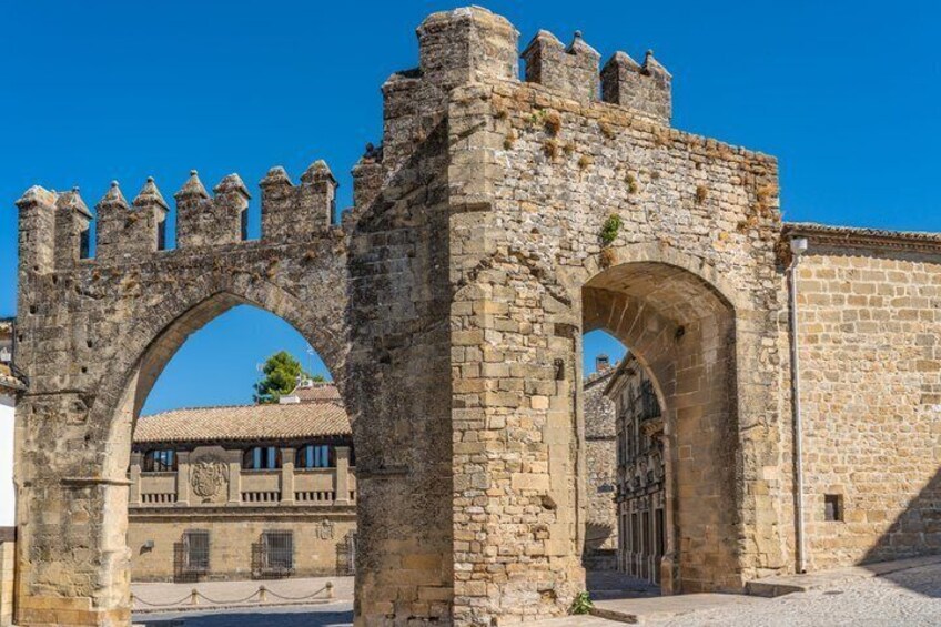 A historic stone archway with battlements, leading to a building with a tiled roof. 3