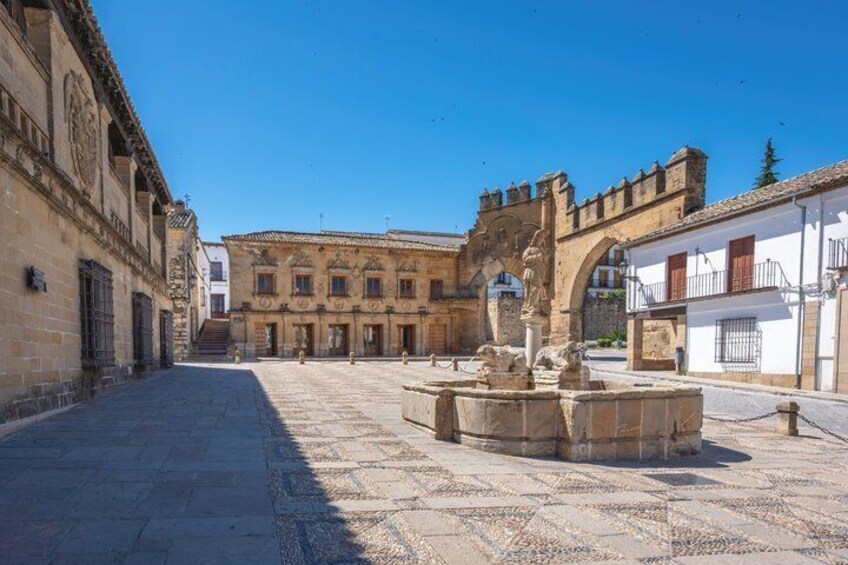 A historic square with a fountain, buildings, and a large archway. 2