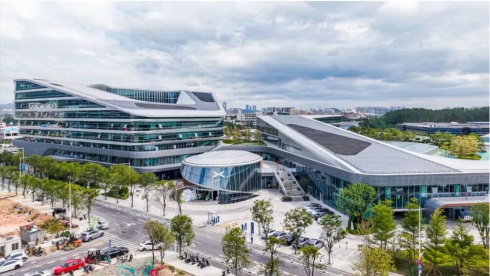 Ein modernes Gebäude mit geschwungener Architektur, umgeben von Bäumen und einer belebten Straße. 2