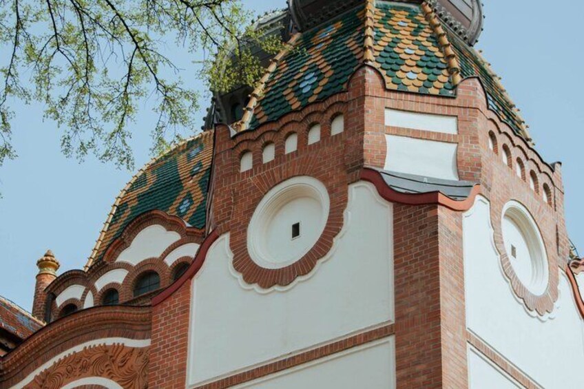 A building with ornate brickwork, circular windows, and a green-tiled roof. 4