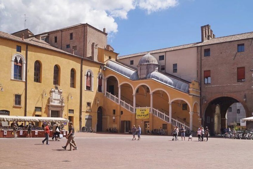 A square with yellow buildings, a staircase, and people walking. 5