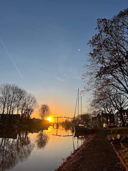 A sunset over a calm river with reflections, leafless trees, and a distant bridge. 1