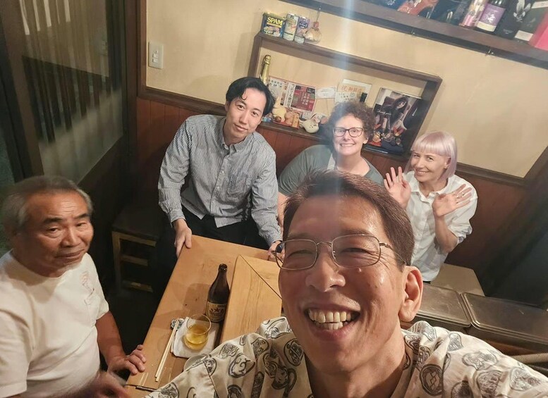 A group of people seated around a wooden table with a bottle and a glass. 2