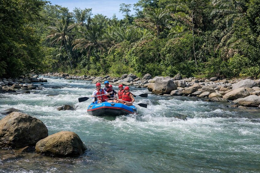 Eine Gruppe von Menschen treibt mit Rafts einen Fluss hinunter, umgeben von Felsen und dichtem Grün. 4