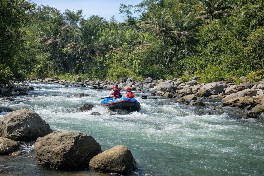 Eine Wildwasser-Rafting-Tour mit zwei Personen in einem blauen Schlauchboot, das einen Fluss zwischen Felsen und dichtem Grün durchfährt. 2