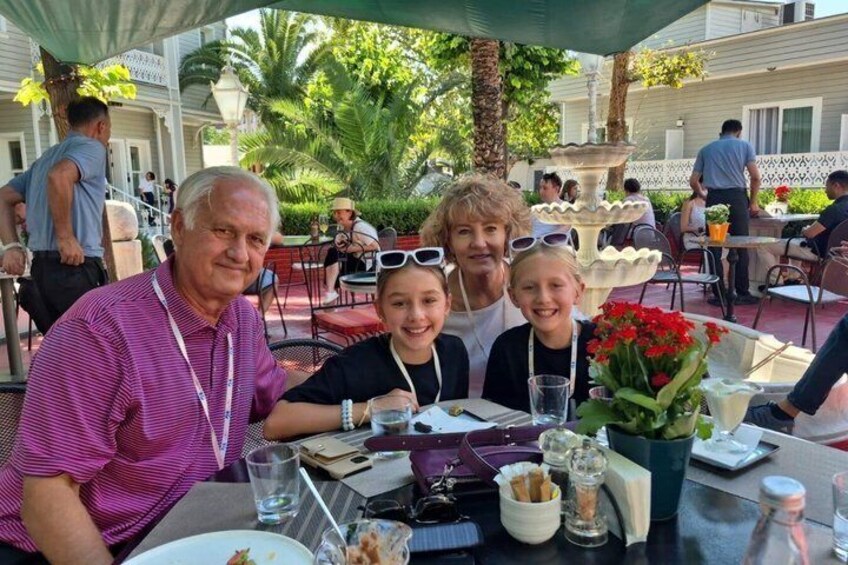 A family dining outdoors with a table, chairs, and a fountain in the background. 2
