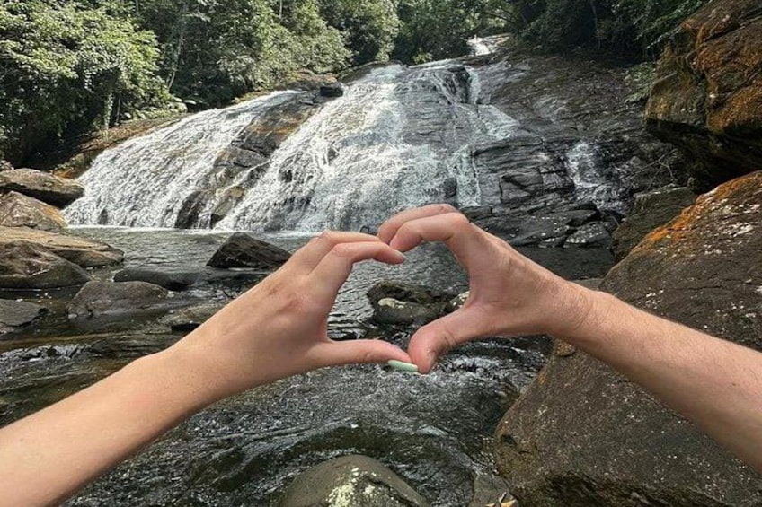 Manos formando una forma de corazón frente a una cascada. 1