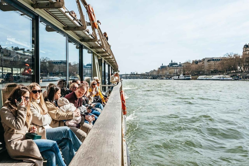 A river cruise with passengers seated along the side, a bridge in the background, and buildings along the riverbank. 4