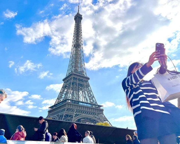 The Eiffel Tower with people taking photos and a clear blue sky. 2