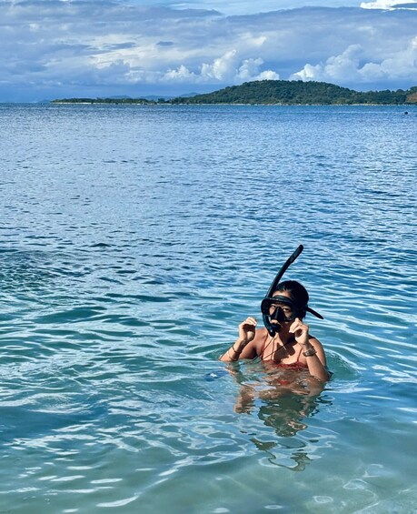 A person snorkeling in clear blue water with a distant island and cloudy sky. 4