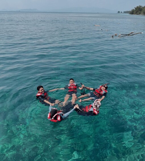 Four people floating in a circle on a calm body of water, wearing life jackets and snorkeling gear. 5